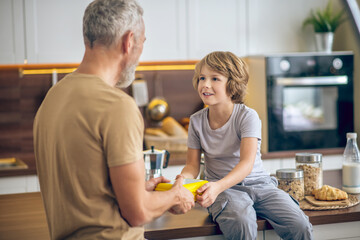 Mature man in beige tshirt and his son in the kitchen at home