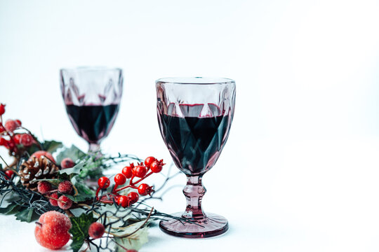 glasses with red wine on a white background and a Christmas branch with berries . serving the festive table