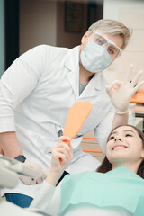 Doctor in white gloves showing okay sign with woman looking in mirror
