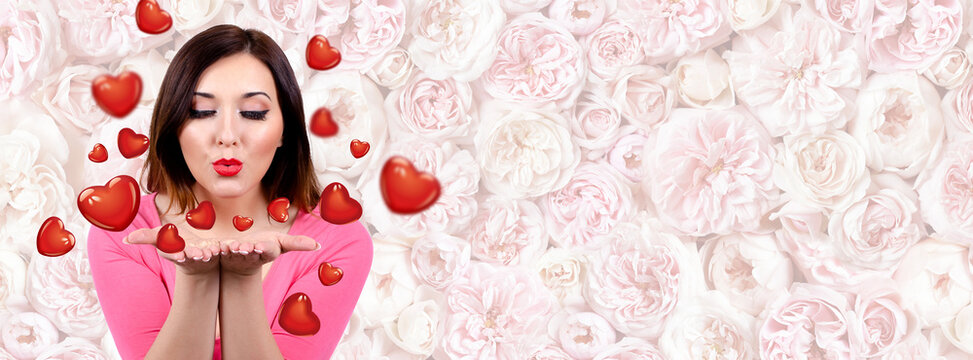 Valentine day, Pretty woman blowing kisses in the shape of a heart. The background is a wall of pink flowers. copy space.