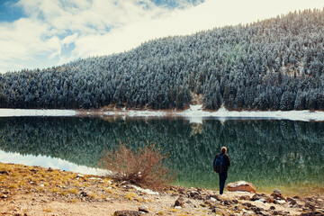 man walk in winter forest covered snow. tourist man travel to snowy mountains background. Winter lake with pine forest and mountains.