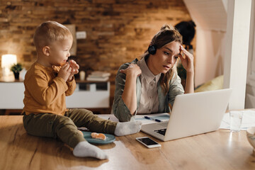 Stay at home mother feeling exhausted while working on laptop at home.