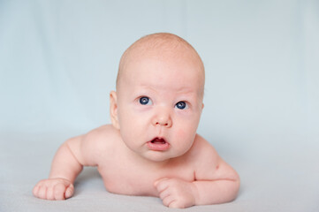 A smiling baby newborn boy with blue eyes smiles and crawls on a white sheet.