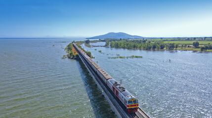 Aerial view of Thailand travel train running into the floating railway bridge with blue sky in the lake of "Pa Sak Jolasid dam" at Lopburi province amazing Thailand. 
