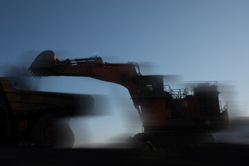 Big dump trucks and excavator in coal mine at sunrise 