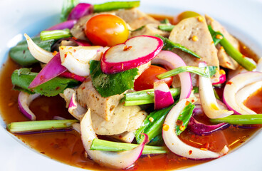 Close up of Thai spicy salad with the ingredients on a white plate on a table.