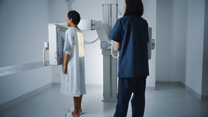 Hospital Radiology Room: Beautiful Latin Woman Standing while Female Radiologist Adjusts X-Ray...