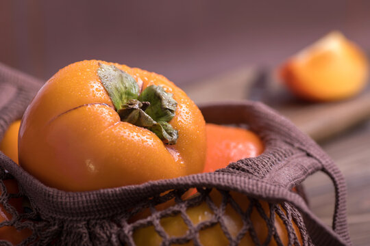 Ripe orange persimmon fruit.Close-up of fresh persimmons in a string bag on a wooden background.