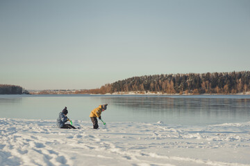 Children in winter clothes play on the shore of a frozen lake.