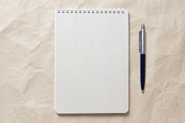  Gray notepad with white coiled spring and pen on a background of beige crumpled craft paper