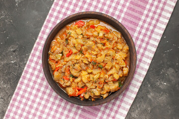 top view roasted eggplant salad in bowl on pink white checkered tablecloth on dark background