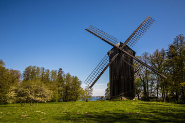 Fototapeta na wymiar Old historic windmill in between green trees, in Estonia, blue sky