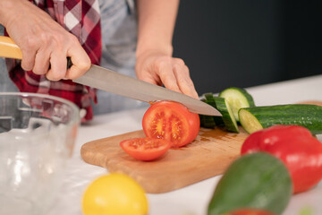 Close up. Woman cutting tomato and cucumber on board preparing vegetables salad for a family dinner standing in the kitchen. Healthy food living. Healthy lifestyle. 