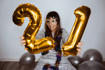 Beautiful woman celebrating the new year with comfortable clothes at home with social distancing. Celebrating 2021 with some golden balloons. 
