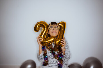Beautiful woman celebrating the new year with comfortable clothes at home with social distancing. Celebrating 2021 with some golden balloons. 