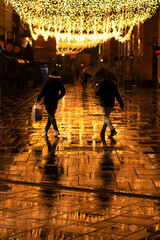 Christmas lights and golden reflections in the city. People at night.  Low light photography with noise and film grain.