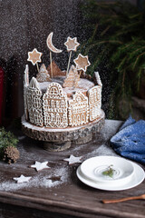 Tall chocolate cake made of thin cakes, decorated with gingerbread, in the form of small houses decorated with white icing.