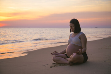 Fototapeta premium Young pregnant Asian woman doing Yoga on the beach at sunset.