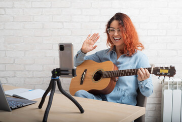 Caucasian woman playing guitar live on a smartphone. The girl leads a music video blog