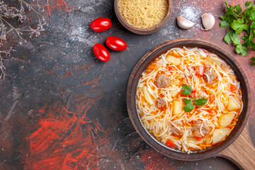 Above view of delicious noodle soup with chicken on wooden cutting board oil bottle and greensgarlic tomato on dark table