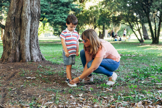 Mom tying sneakers to her little son. Mother with her child in the middle of forest park.