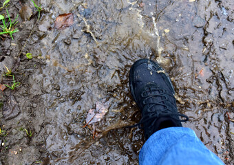 Water splash from shoes. Men's feet in hiking shoes steps into a puddle. Rain footwear for man or woman. Trekker boots for for cold and weather hike. Pair of waterproof travel shoe in blue jeans