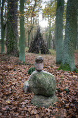 Mystical shot of a stone cairn in the woods with a wooden stack of branches in the background