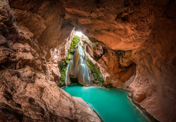 A beautiful waterfall inside a cave and a lake of crystal clear turquoise water. Enchanted landscape, a cave inside a mountain in which there is a waterfall and a crystalline river. Bercolon waterfall