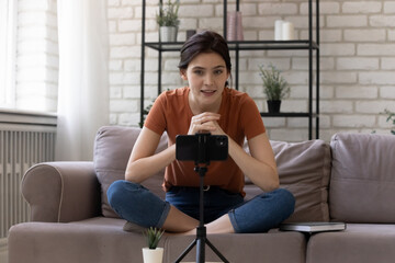 Vlogger influencer. Young woman blogger sitting cross-legged on sofa at home recording clip content...