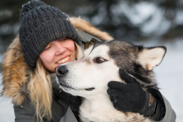 Smiling woman embracing alaskan malamute with love in winter forest . close up.