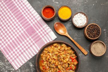 top view roasted eggplant salad in bowl wooden spoon different spices in bowls kitchen towel on dark background