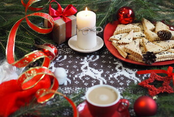 Blurred foreground. Cup of hot coffee with homemade shortbread cookies and red Christmas decor on a knitted knitted background with deer. Congratulatory background.