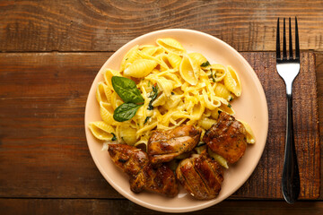 A plate of pasta in a creamy sauce with cheese and chicken on the table next to the fork.