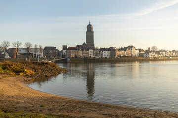 Beach lit up by early morning sun in the foreground and cityscape of the Dutch Hanseatic medieval city of Deventer in The Netherlands seen from the other side of the river IJssel behind