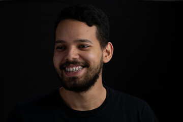 Obraz premium Young bearded man headshot over black background. He looks happy with a big smile.