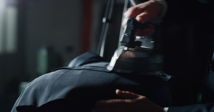 Cinematic close up shot of experienced tailor is ironing fine quality fabric for creation custom haute couture apparel in traditional tailoring atelier. Concept of handmade, couturier and tradition.