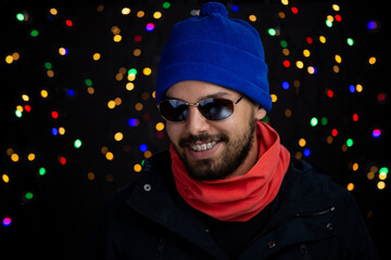 Young man headshot with happy expression with Christmas lights in background.