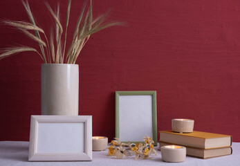 old books, candles are burning, a gray vase with ears of corn, dry daffodils, photo frames on a red background