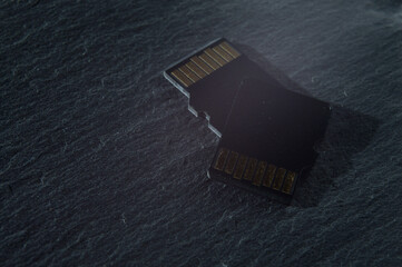 two micro sd cards lie on top of each other on a dark textured background, with golden contacts at...