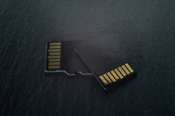 two micro sd cards lie on top of each other on a dark textured background, with golden contacts at...