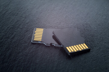 two micro sd cards lie on top of each other on a dark textured background, with golden contacts at...