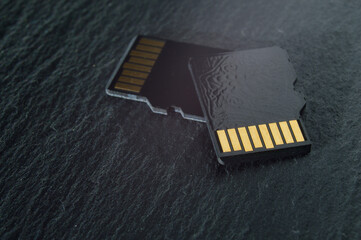 two micro sd cards lie on top of each other on a dark textured background, with golden contacts at...