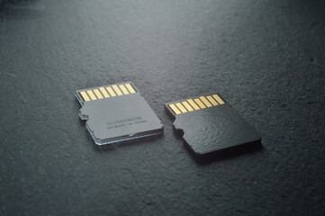 two micro sd cards lie on a dark textured background, with golden contacts at the top. close-up.