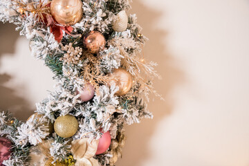 Christmas wreath made of natural fir branches hanging on a beige wall. Wreath with natural ornaments: bumps, walnuts, cones. New year and winter holidays.Christmas decor. traditional wreath.Copy space