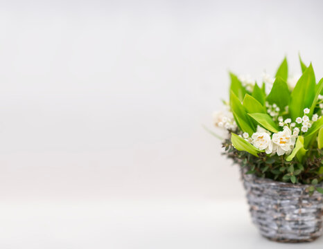 Cute little floral arrangement of flowers in wood basket on light background. stock photo. 
Basket with bouquet of lilly-of-the-valley and daffodils
