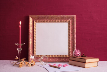 old books, a candlestick on a long leg with a burning candle, an old photo frame on red and a decor...