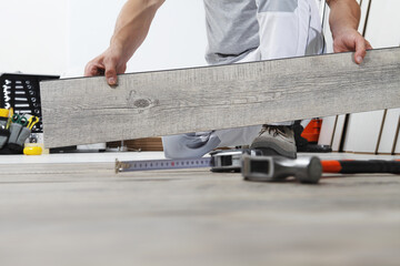 Worker hands installing timber laminate vinyl floor. Wooden floors house renovation.