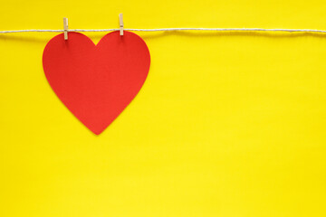 Red heart hanging on rope with small clothes pins on yellow background. 