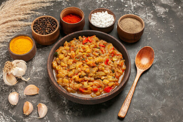 bottom view roasted eggplant salad in bowl different spices in bowls wooden spoon garlic on dark background