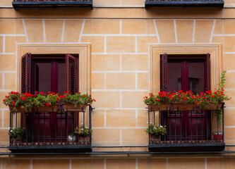 Two small balconies with flowerpots on railings at light brown facade residential building. Madrid old town urban area